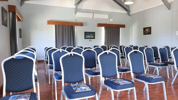 A conference room with rows of blue chairs, wooden beams, and a ceiling fan.