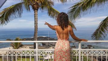 A person standing on a balcony with a view of the ocean and palm trees.