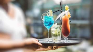 A person holding a tray with two drinks, one blue and one red, each with a straw and garnish.