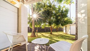 A patio with two white chairs and a small table, surrounded by a stone wall and trees. - Hôtel Exsel Alamanda (Saint-Paul)