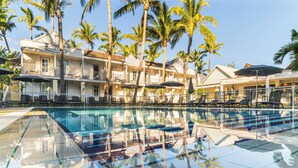 A pool area with clear water, surrounded by palm trees and a building with multiple balconies. - Hôtel Exsel Alamanda (Saint-Paul)