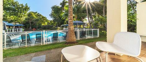 A pool area with clear glass barriers, a palm tree, and outdoor seating.