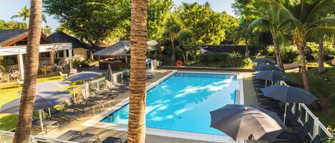 Ein Swimmingpool mit Liegestühlen und Sonnenschirmen, umgeben von Palmen und viel Grün.