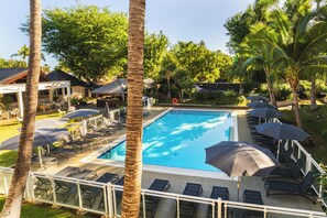 A swimming pool with lounge chairs and umbrellas, surrounded by palm trees and greenery. - Hôtel Exsel Alamanda (Saint-Paul)