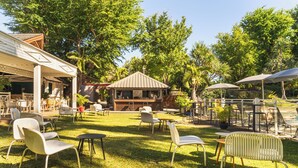 An outdoor patio area with multiple seating arrangements, including chairs and tables, surrounded by lush greenery and trees. - Hôtel Exsel Alamanda (Saint-Paul)