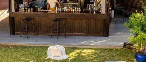 An outdoor bar area with a metal roof, surrounded by a grassy lawn and white chairs.