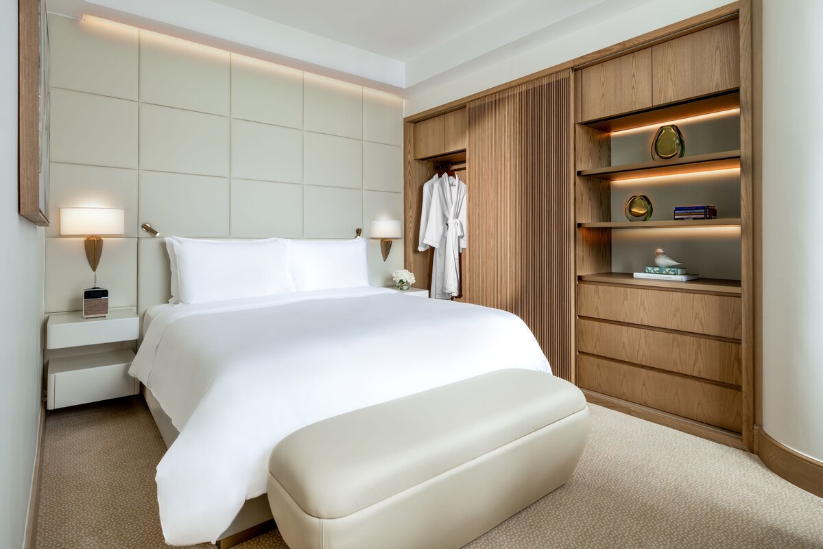 Une chambre d’hôtel avec un grand lit, des lampes de chevet, une armoire en bois et une petite table avec une lampe.