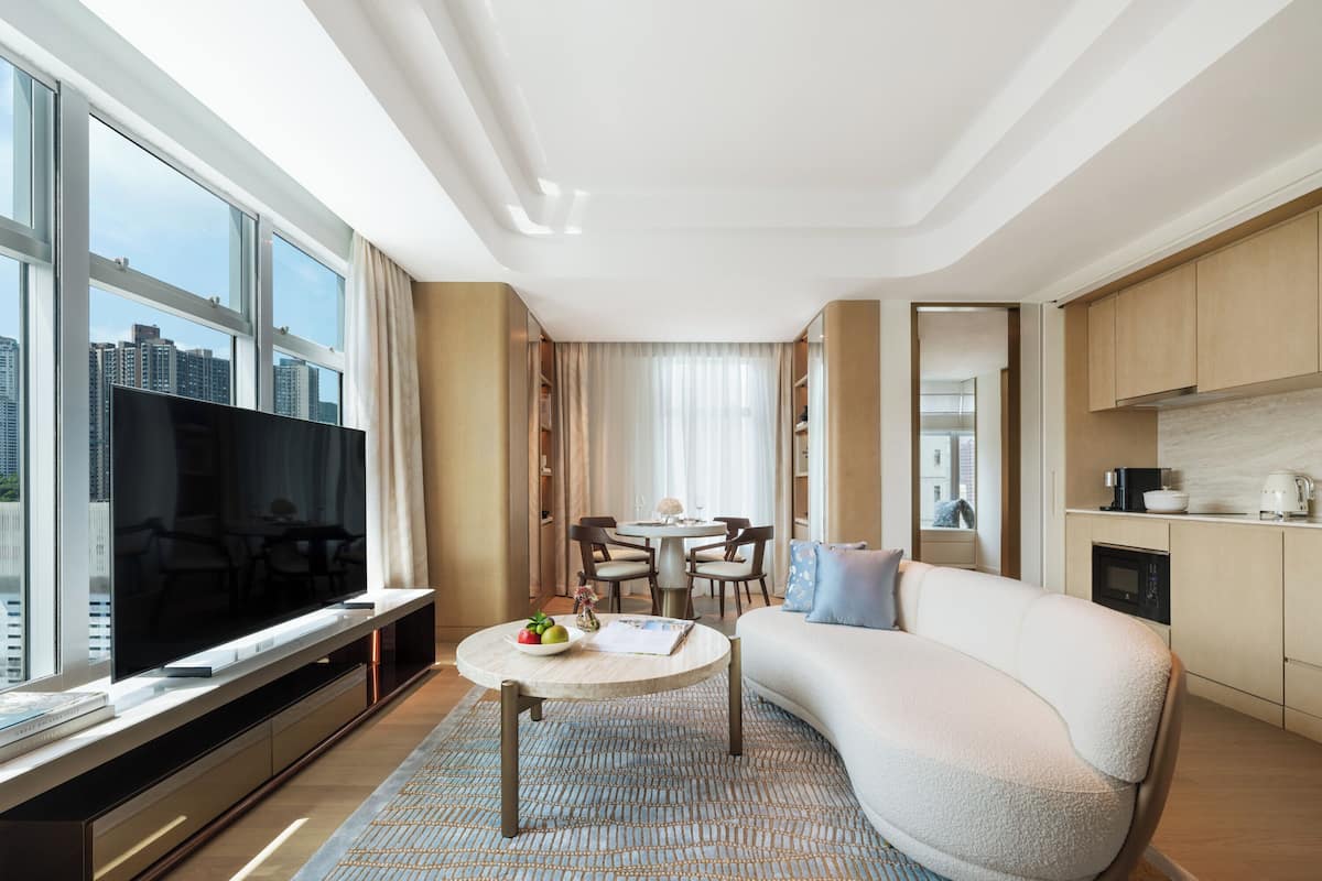 A modern hotel room with a large TV, a dining area, and a kitchen.