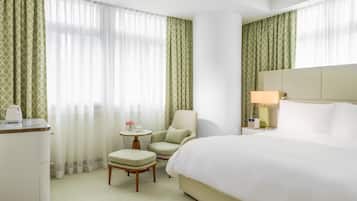 Een hotelkamer met een bed, een stoel, een klein tafeltje met een lamp en een bureau met een waterkoker.