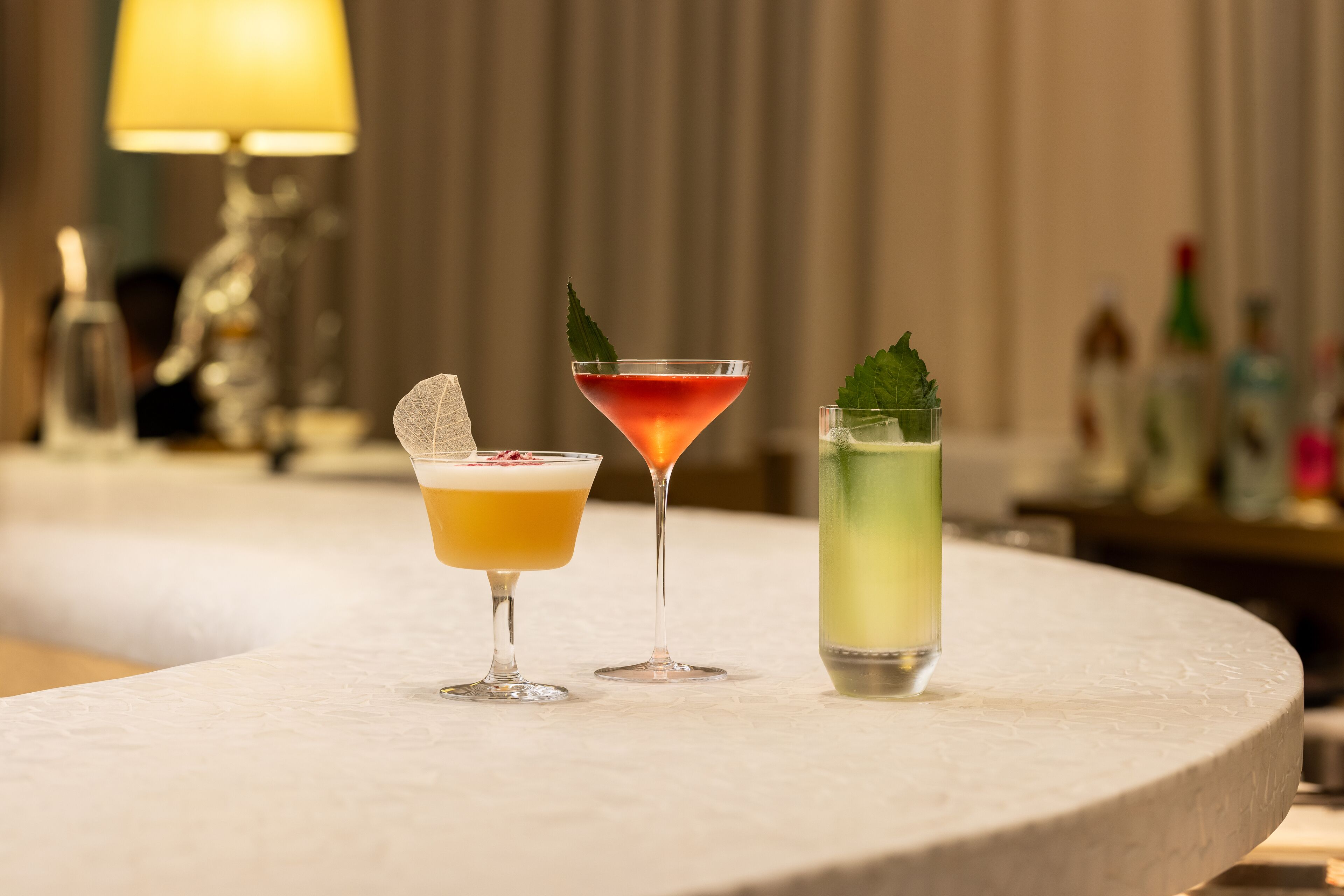 Three cocktails on a round table with a blurred background of a bar area.