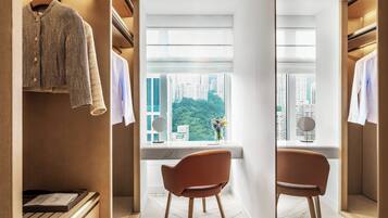 A modern hotel room with a walk-in closet, a seating area with a view of the city, and a large window.