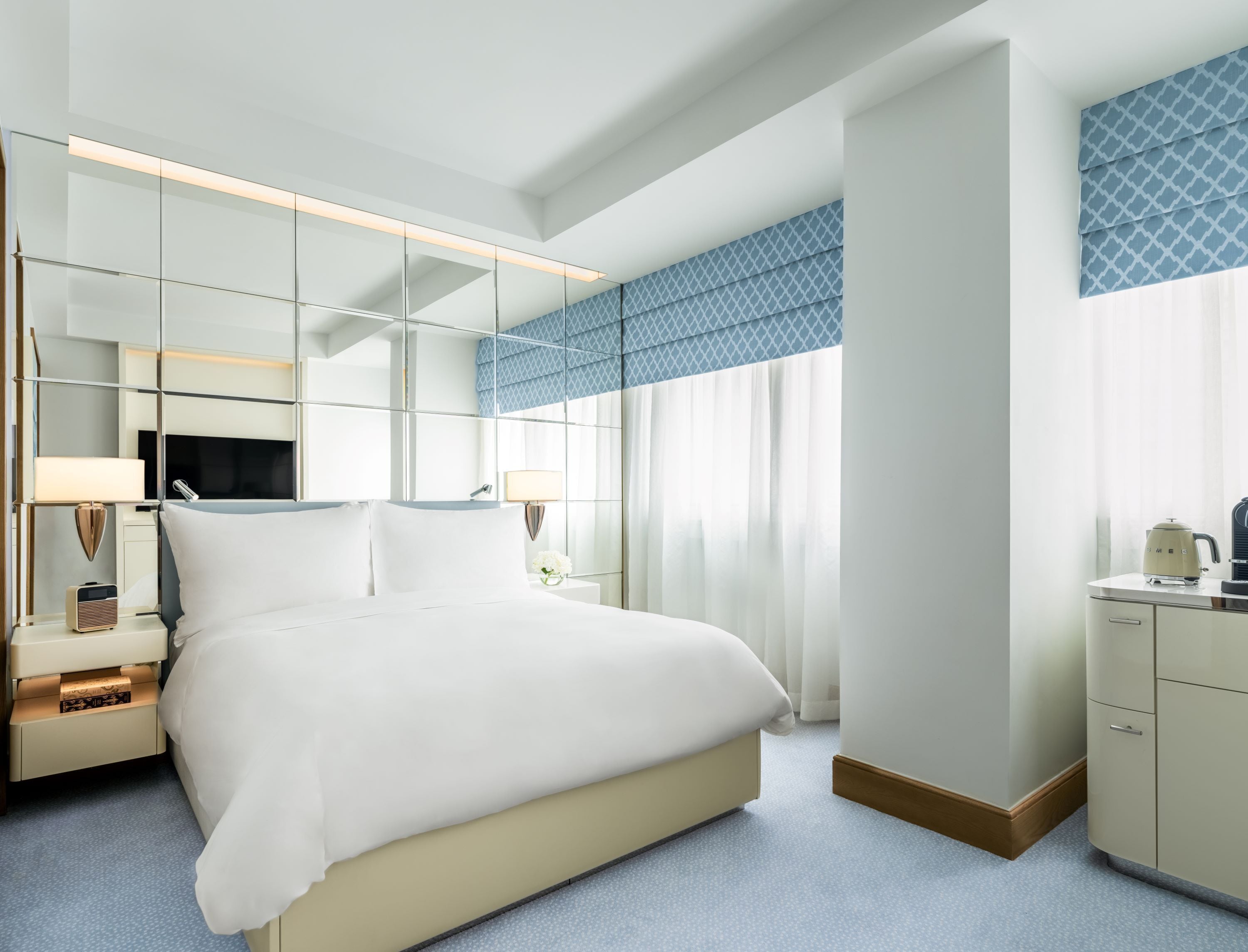 A modern hotel room with a large bed, a television, a bedside table, a lamp, and a wardrobe.