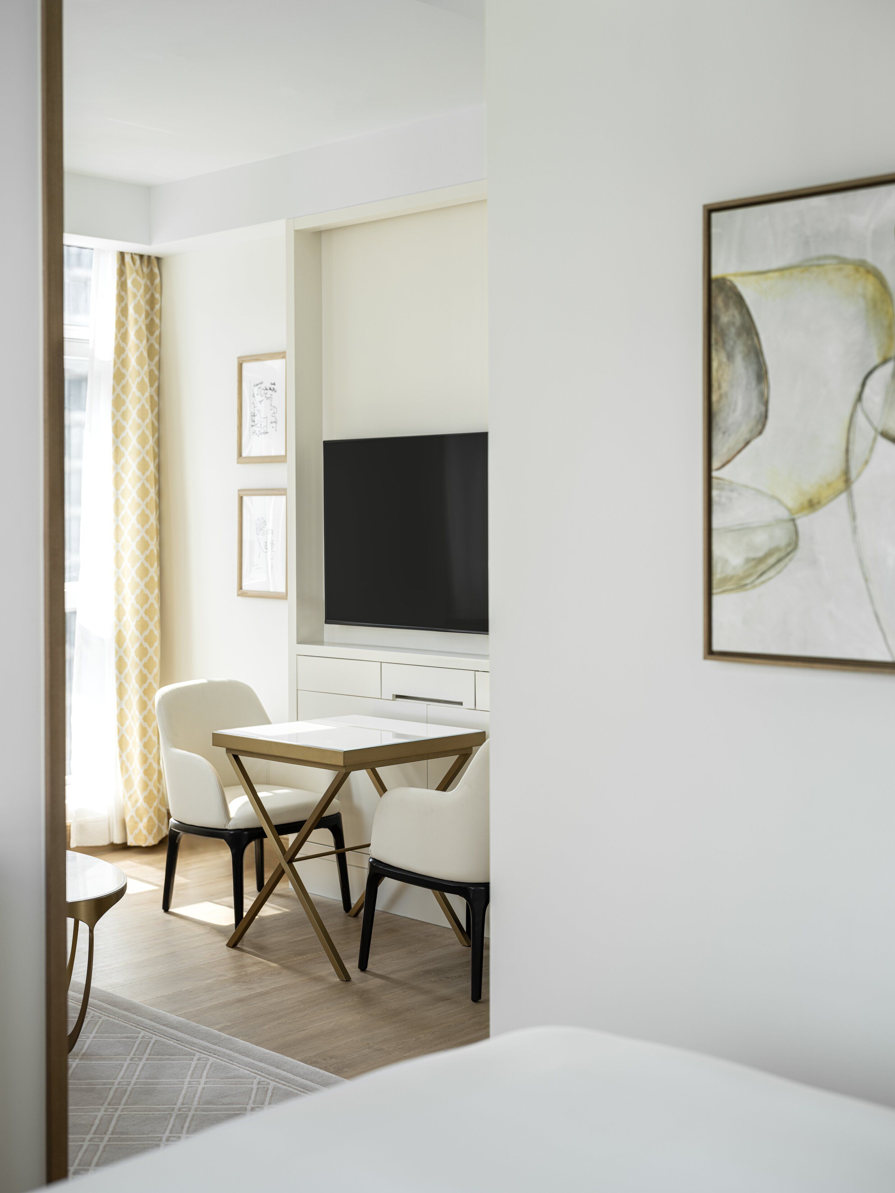 Une pièce moderne et minimaliste comprenant un coin repas, un téléviseur à écran plat fixé au mur et une œuvre d’art abstraite encadrée.