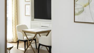 Une pièce moderne et minimaliste comprenant un coin repas, un téléviseur à écran plat fixé au mur et une œuvre d’art abstraite encadrée.