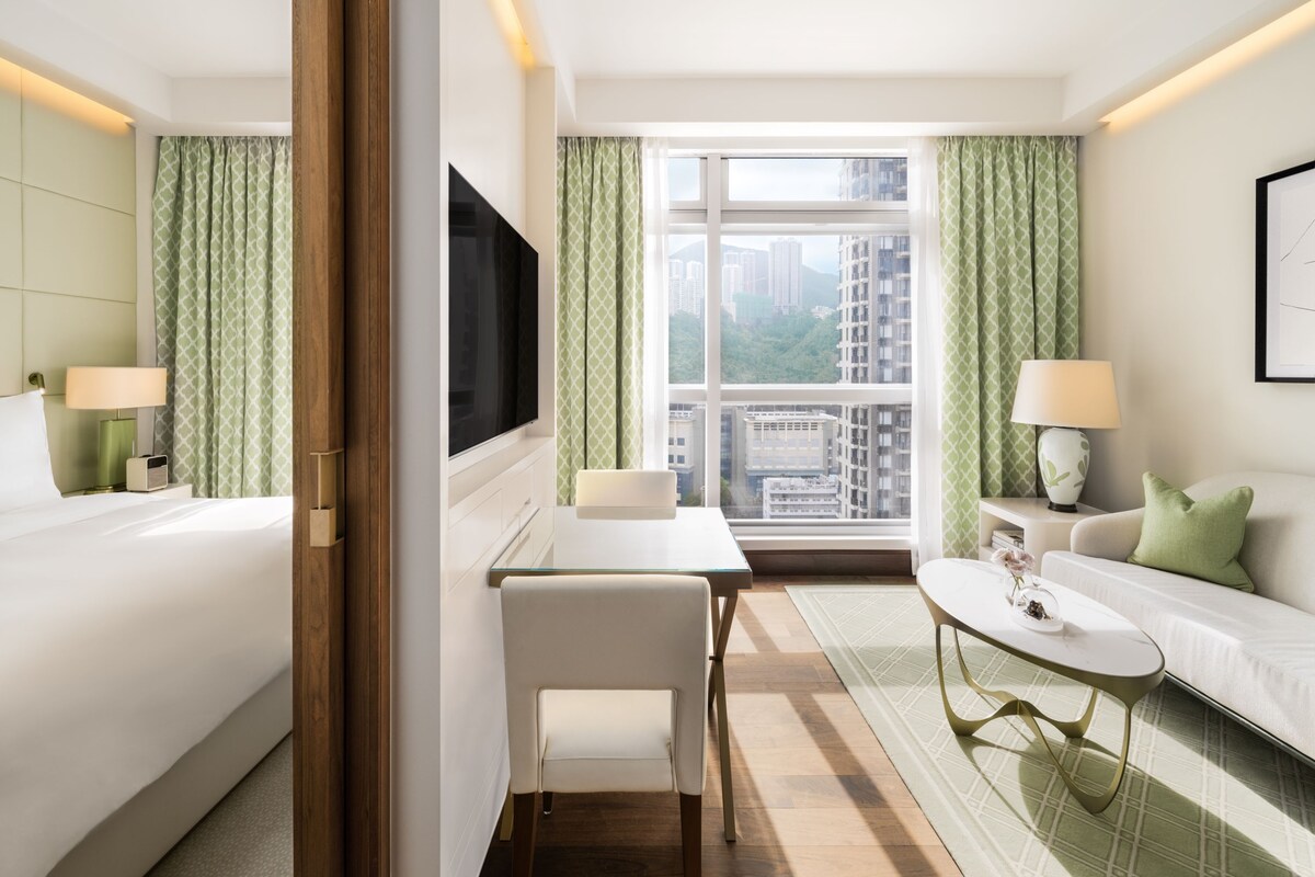 Une chambre d’hôtel comprenant un lit, un bureau, une chaise, un canapé, une télévision et une fenêtre donnant sur la ville.