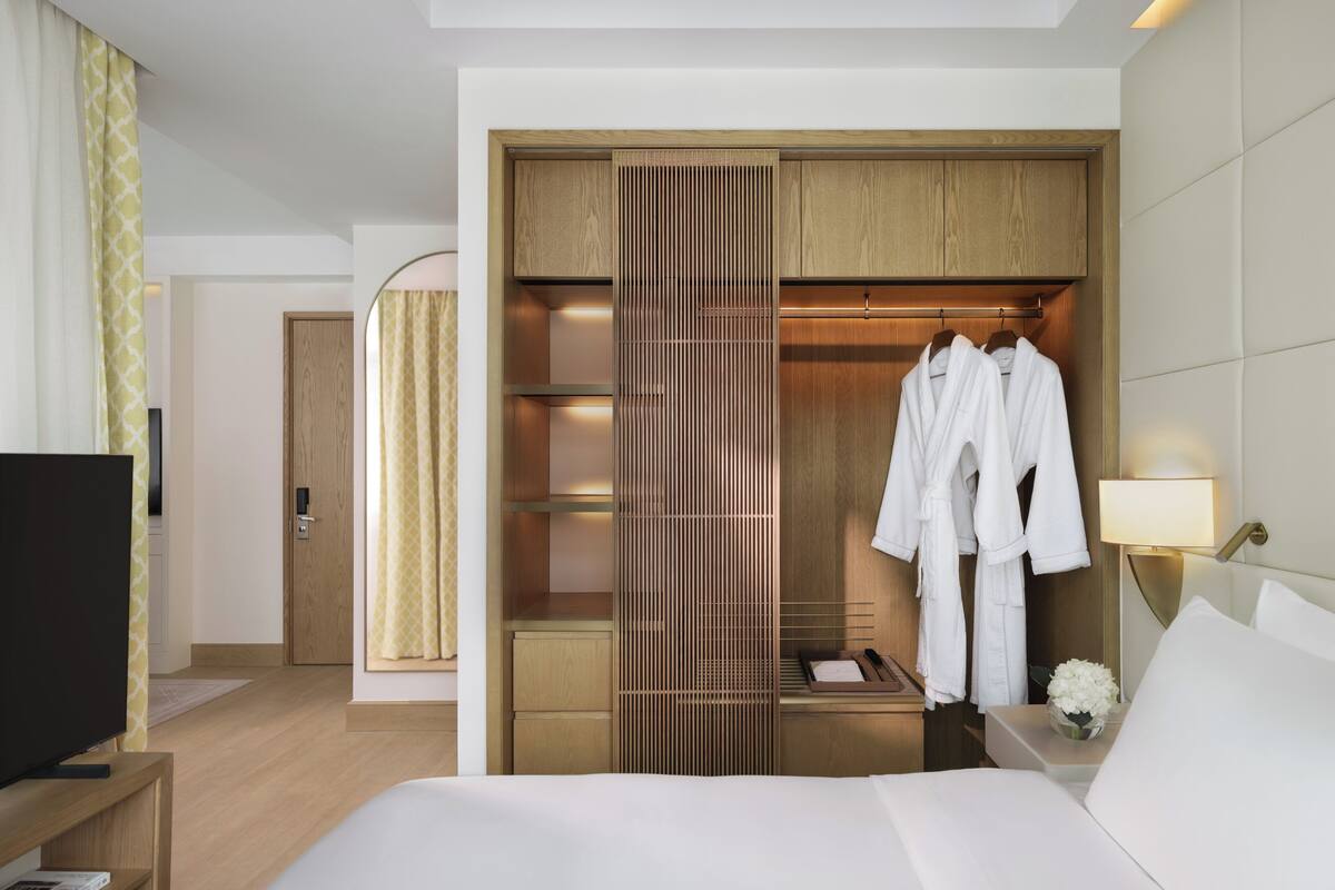 A hotel room with a large bed, a TV, a wardrobe, and a bedside table with a lamp.