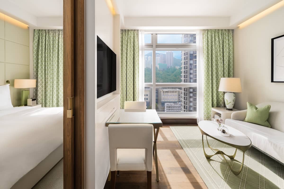 A hotel room with a bed, a desk, a chair, a sofa, a TV, and a window with a city view.