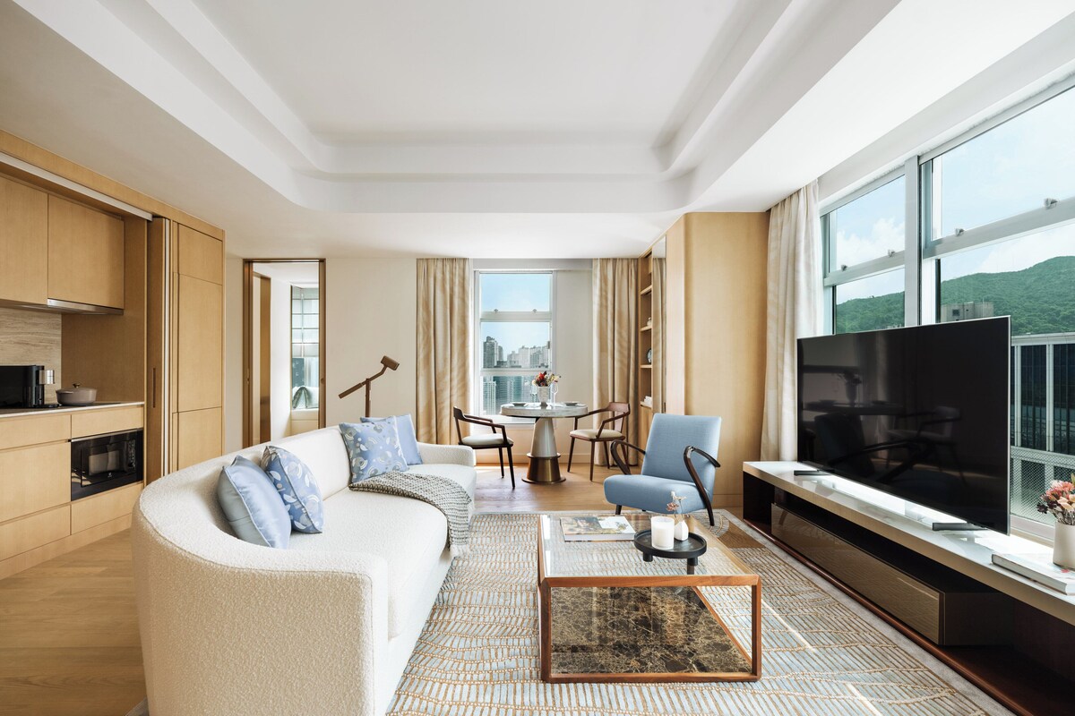 A modern living room with a sofa, a coffee table, a TV, and a city view through large windows.