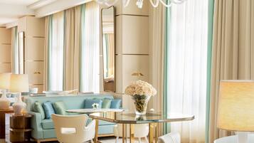 A spacious living room with a chandelier, a blue sofa, a round glass table, and a large mirror.