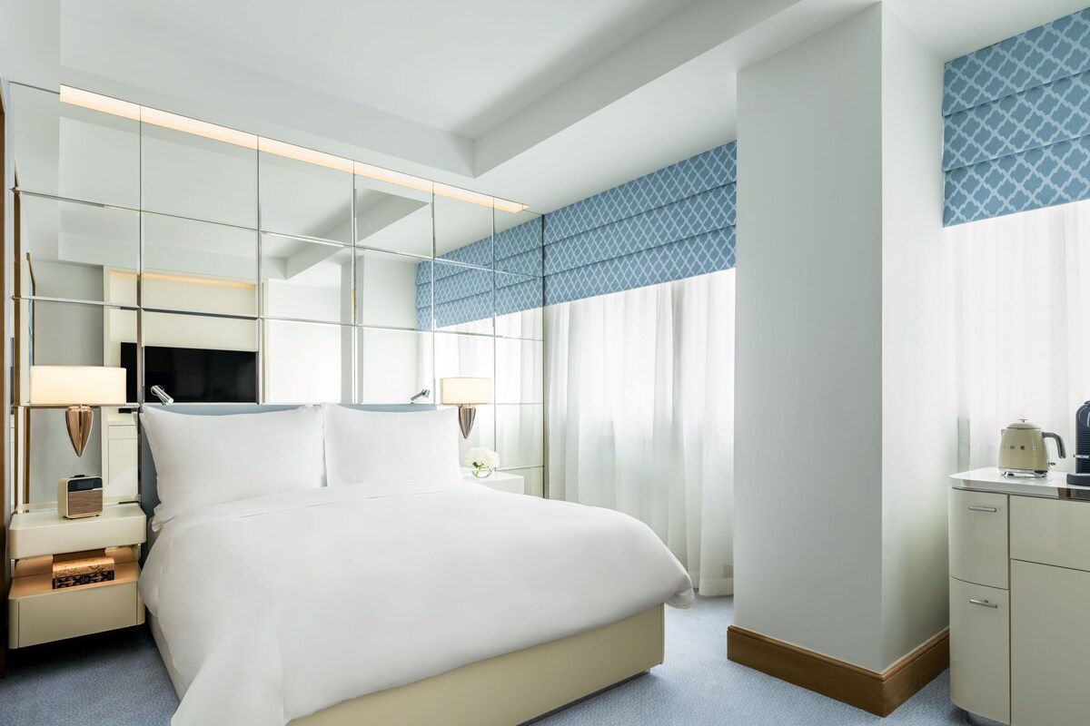 Une chambre d’hôtel moderne équipée d’un grand lit, d’une télévision, d’une table de chevet, d’une lampe et d’une armoire.