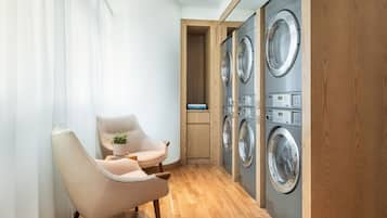 Une buanderie avec un plancher en bois, un fauteuil beige et une rangée de machines à laver à chargement frontal, les unes superposées aux autres.