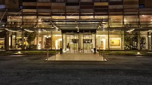 Una entrada de hotel moderna con fachada de vidrio, un paseo techado y un jardín ajardinado.