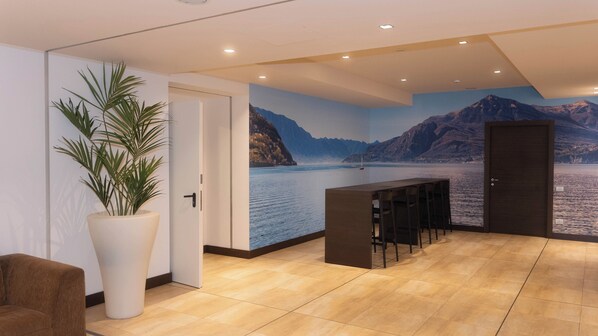 Un interior moderno con una planta grande en maceta, una zona de bar y un mural con un lago y montañas.