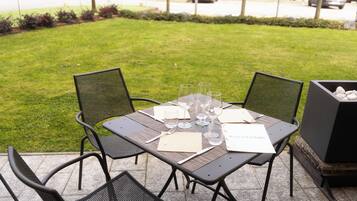 Ein Essbereich im Freien mit einem Tisch für vier Personen, umgeben von Stühlen, auf einer Terrasse mit einem Rasen im Hintergrund.