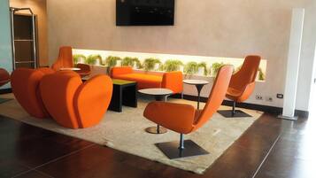 A modern lounge area with orange seating, a flat-screen TV, and a view of greenery.