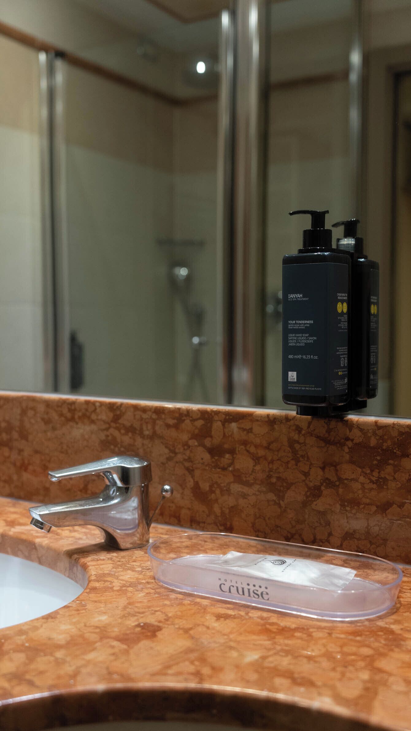 A bathroom with a marble countertop, a sink, a mirror, and a bottle of hand soap.