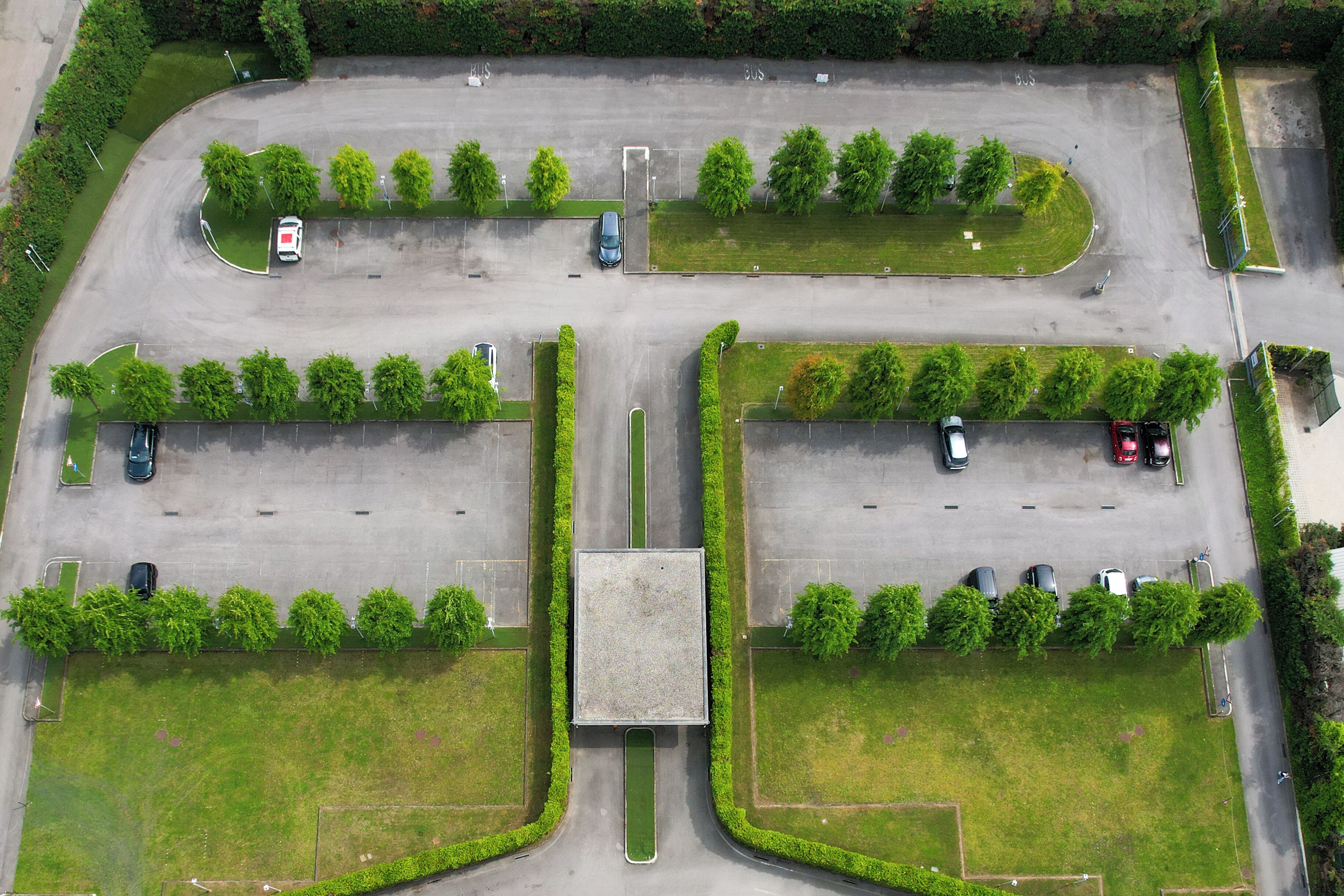 An aerial view of a parking lot with multiple rows of parked cars, green landscaping, and a central square.