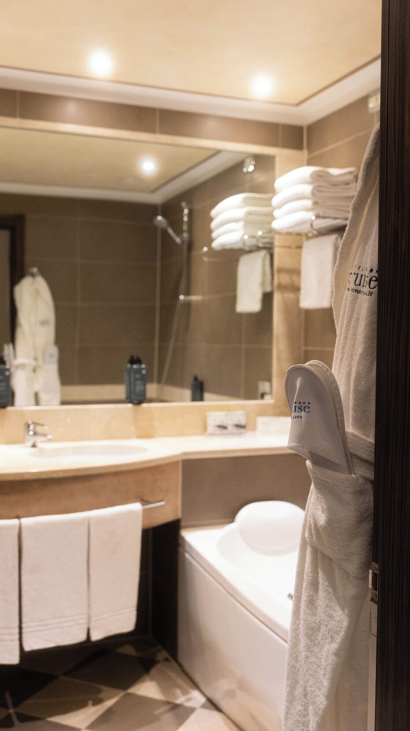 Un baño moderno con un espejo grande, una bañera y un lavamanos. Se ven toallas y artículos de aseo.