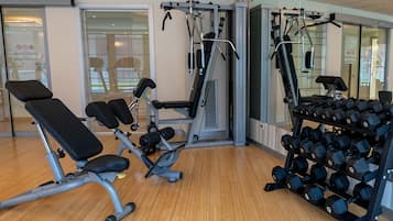 Un gimnasio con equipo de ejercicio, que incluye una banca, máquinas de pesas y un estante con mancuernas.