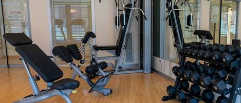 A gym with exercise equipment, including a bench, weight machines, and a rack of dumbbells.