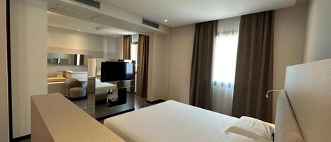 A modern hotel room with a large bed, a flat-screen TV, a desk, and a seating area.