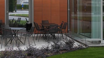 An outdoor seating area with a table and chairs under a white umbrella, adjacent to a building with a glass entrance.