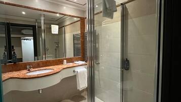 Ein modernes Badezimmer mit einer Duschkabine aus Glas, einer Marmorplatte und einem großen Spiegel.