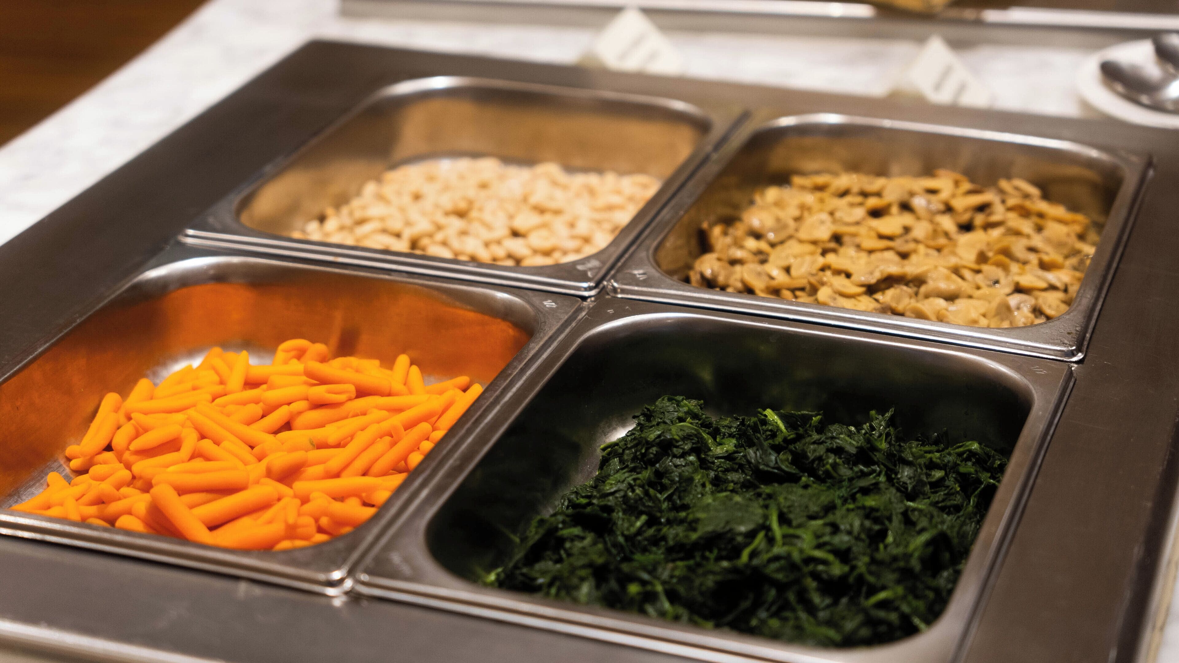 Ein Buffet mit vier Metalltabletts, auf denen verschiedene Speisen angeordnet sind.