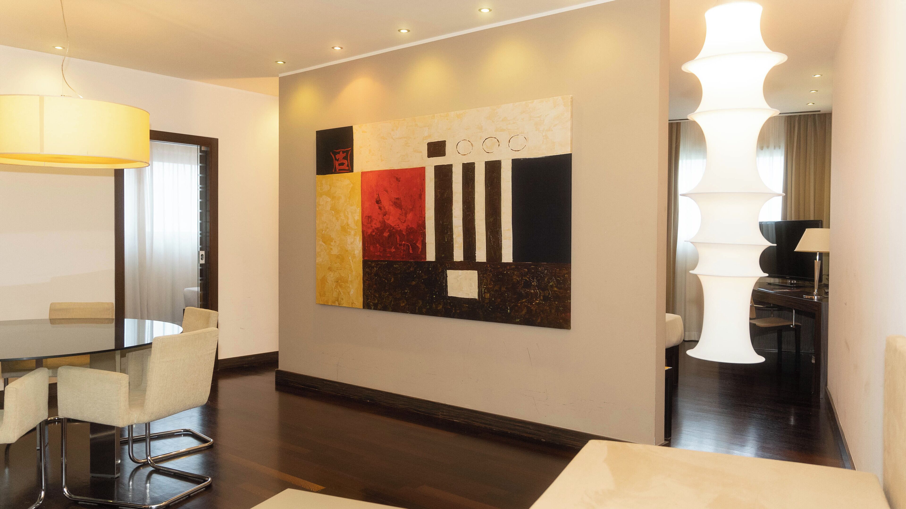 Een moderne hotelkamer met een zithoek, een groot abstract schilderij aan de muur en een grote witte lamp.