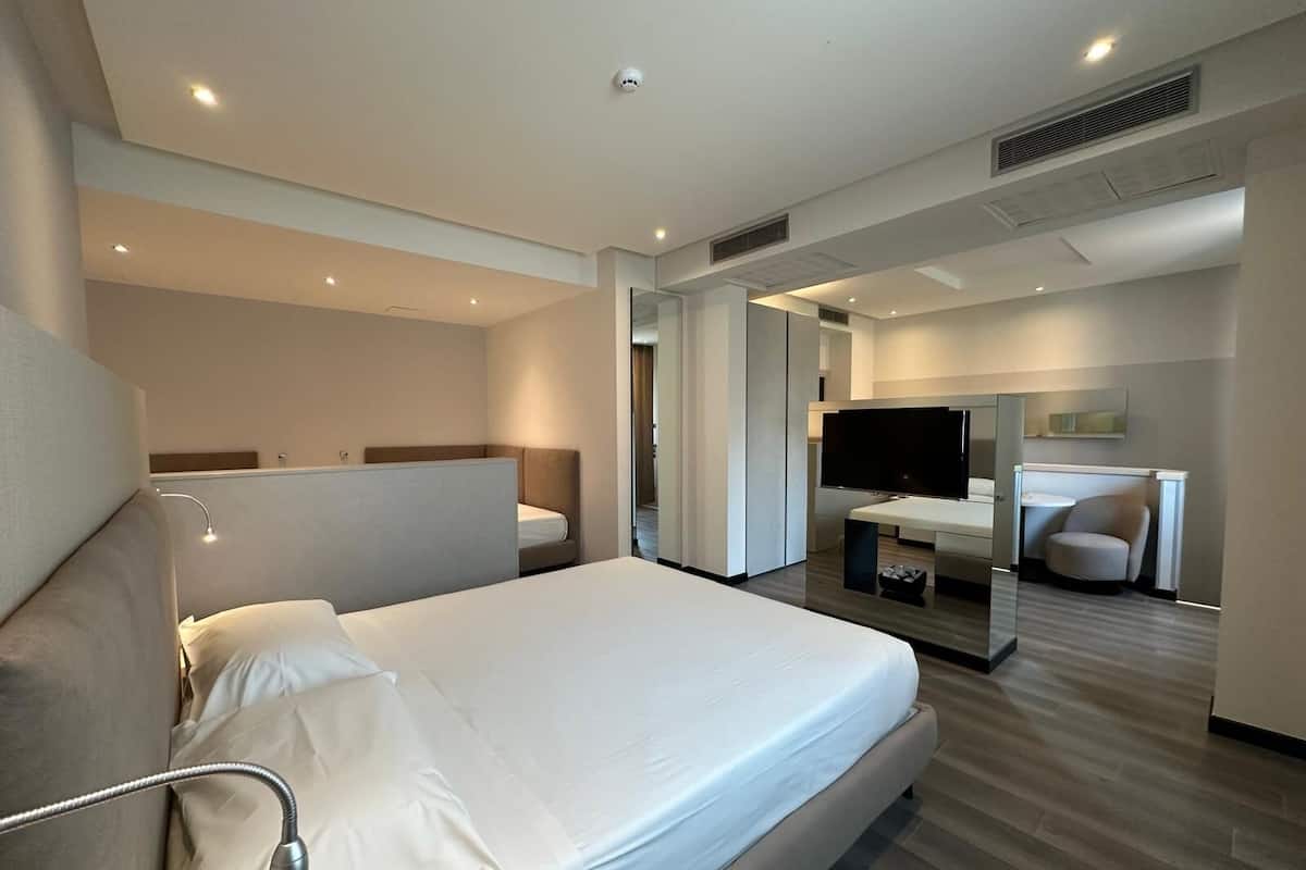 A modern hotel room with a large bed, a desk, a television, and a seating area.
