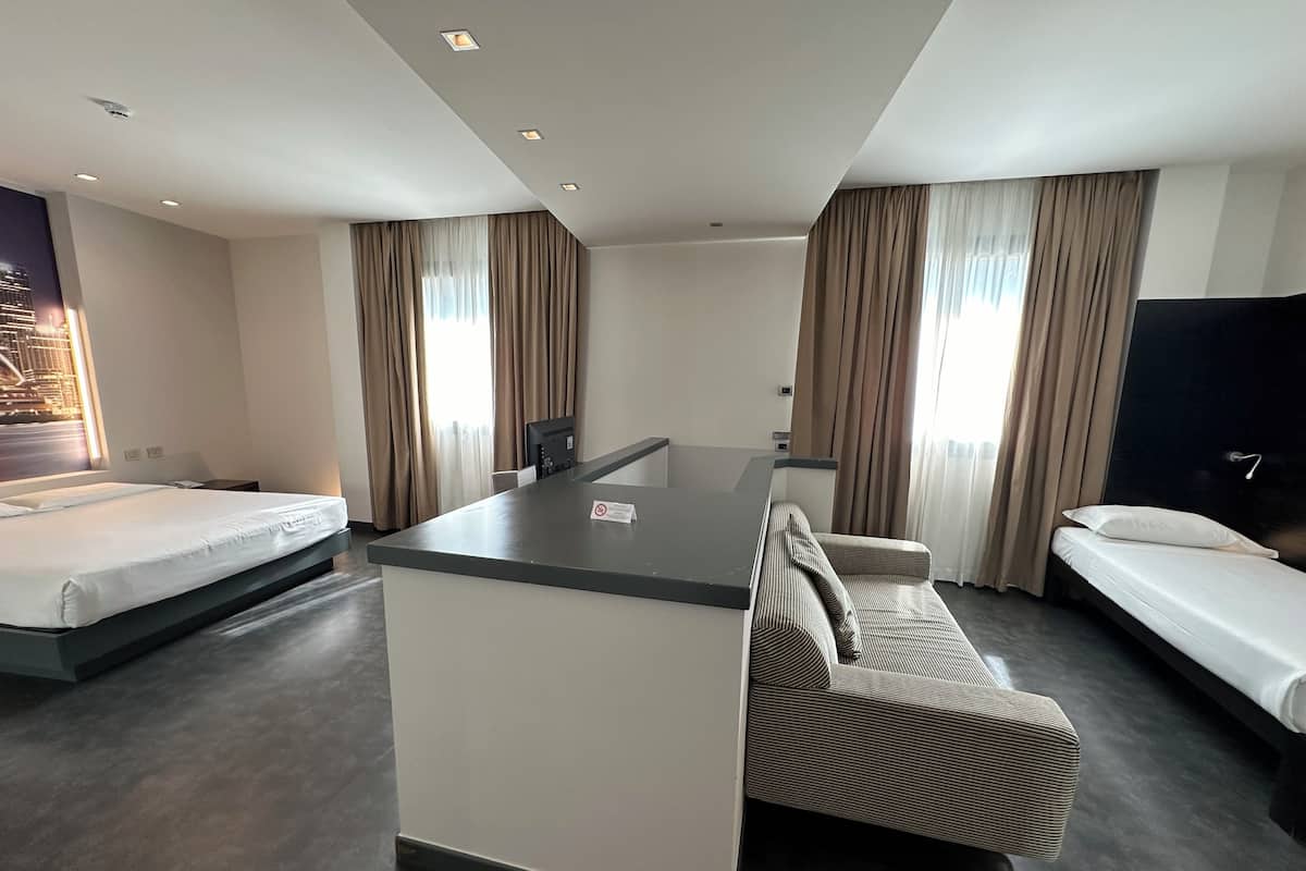 A modern hotel room with a central island, two single beds, a sofa, and a TV.