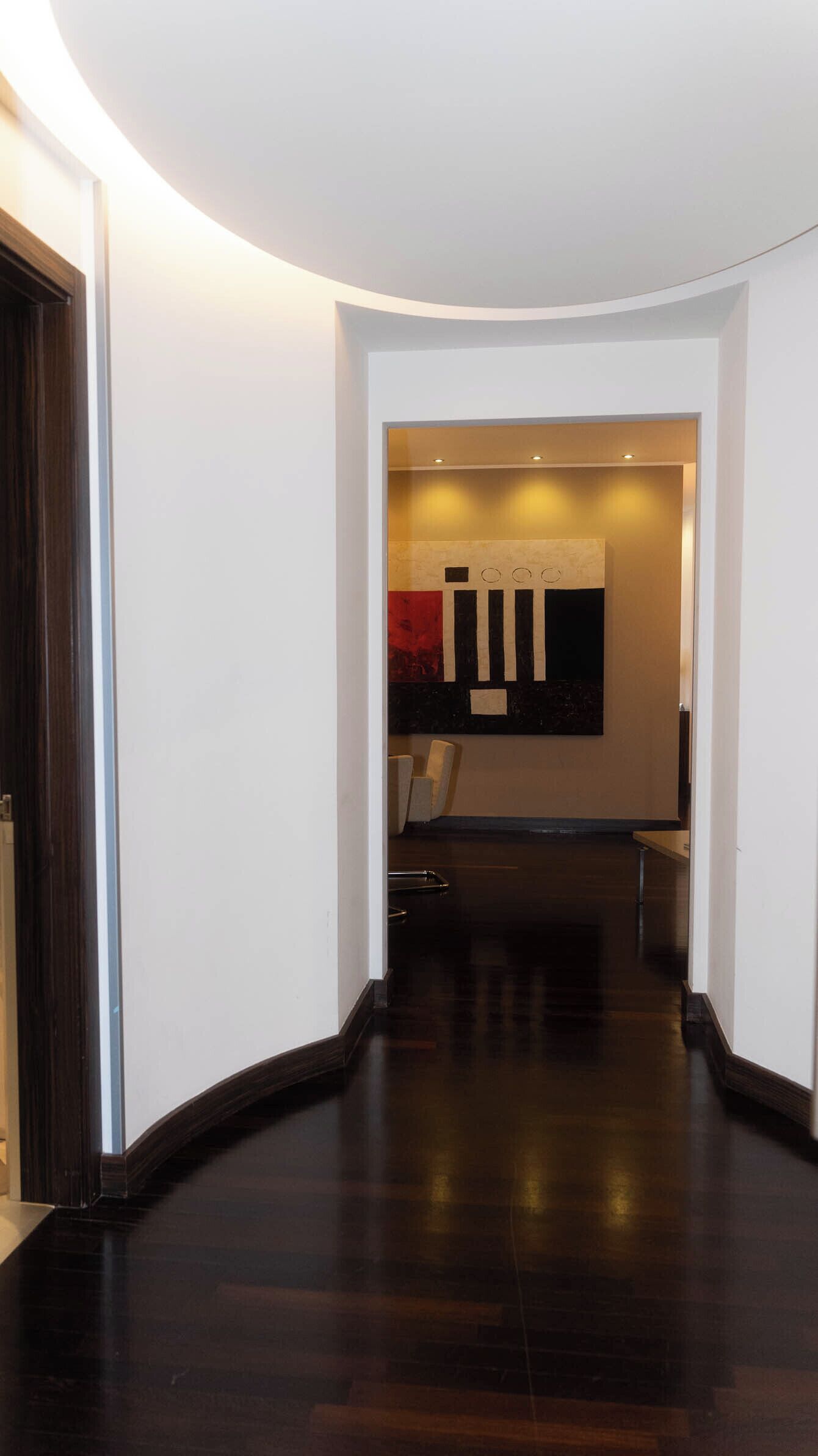Un pasillo con suelo de madera oscura, paredes blancas y un foco empotrado en el techo.
