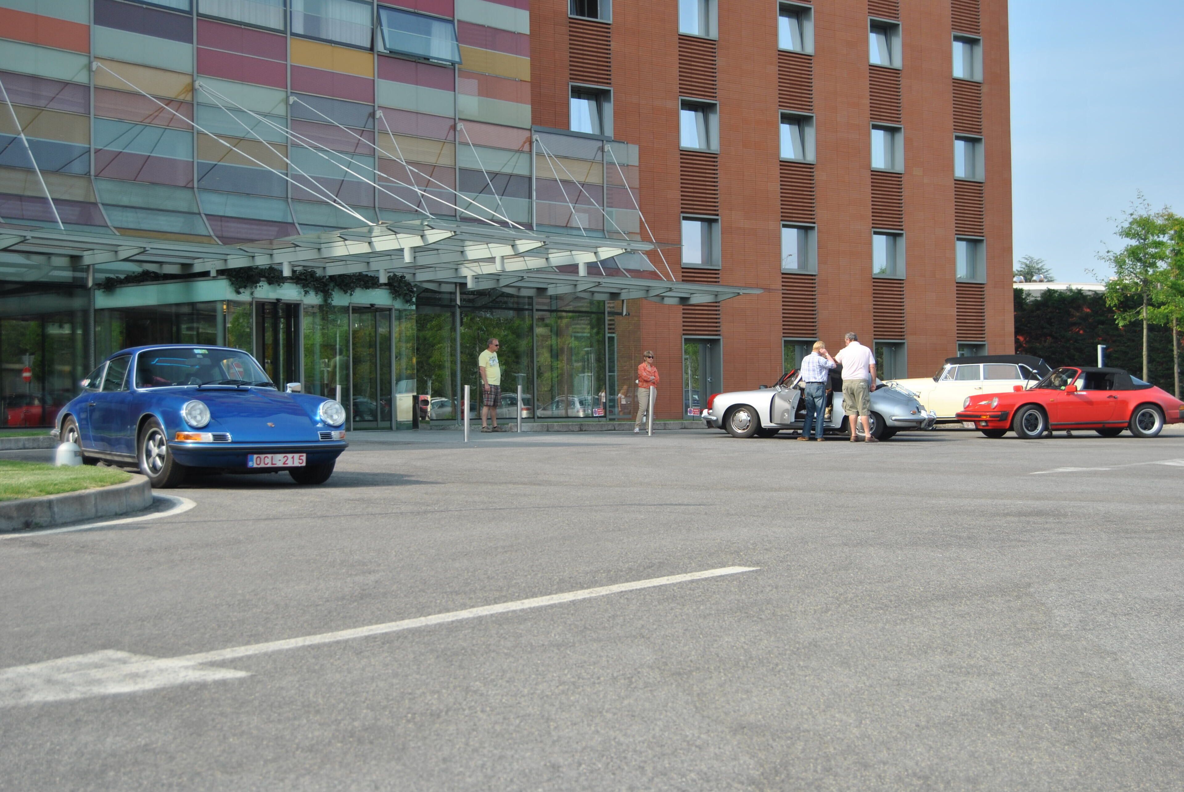 A modern building with a glass entrance and a parking area with several classic cars.