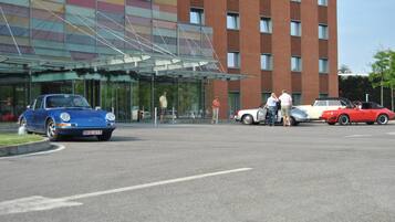 Ein modernes Gebäude mit Glastür und Parkplatz, auf dem mehrere Oldtimer geparkt sind.