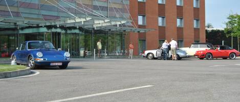 A modern building with a glass entrance and a parking area with several classic cars.