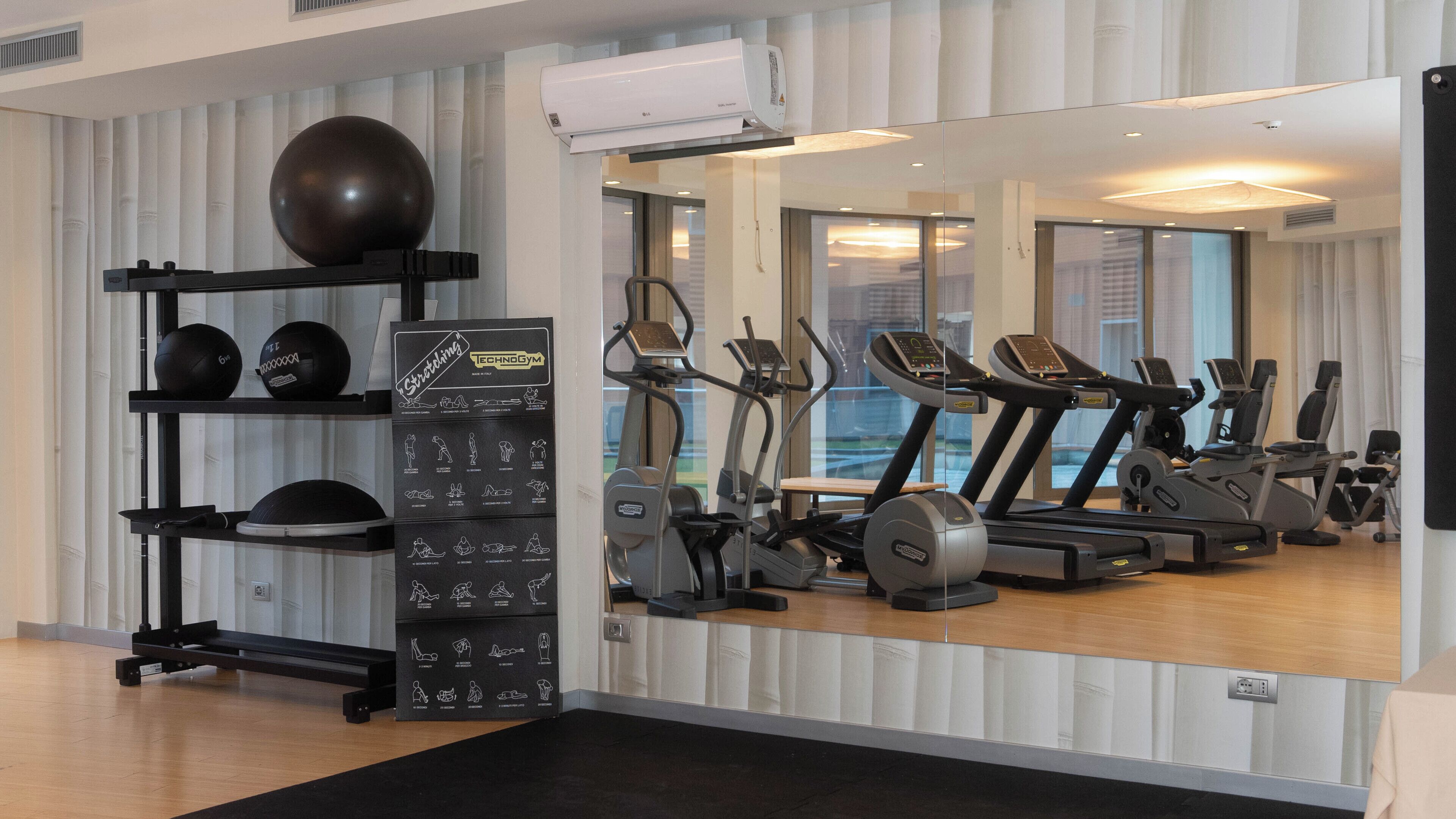 Uma academia com equipamentos de exercícios, um espelho e um grande aparelho de ar condicionado.