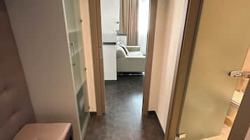 Una habitación de hotel con una cama, un banco, un ventanal y vista a otra habitación.