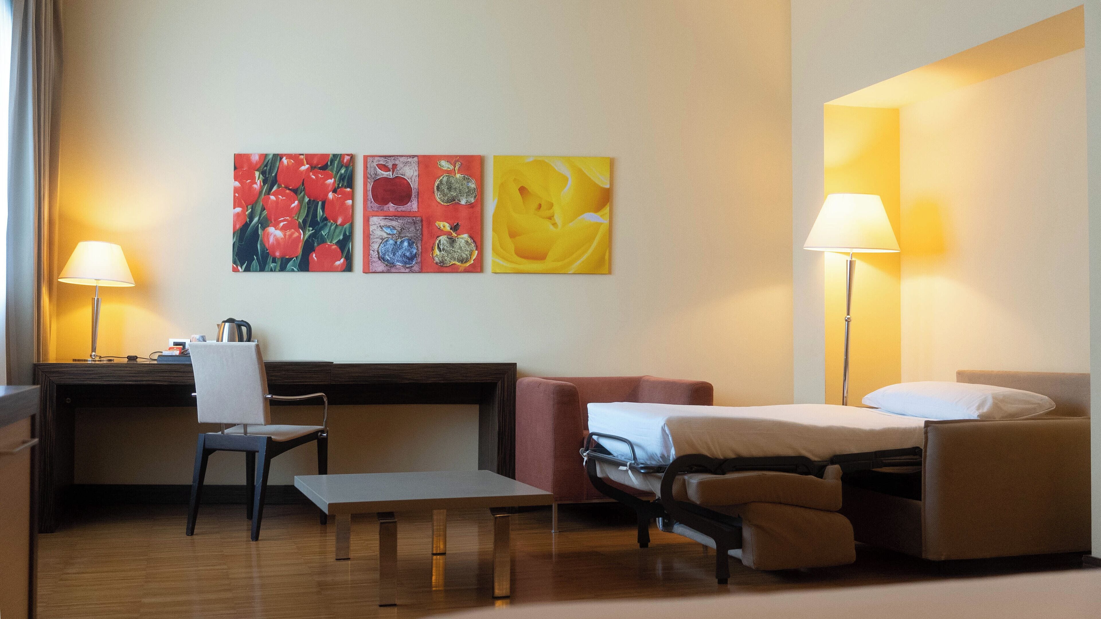 A hotel room with a desk, chair, bed, and two lamps.