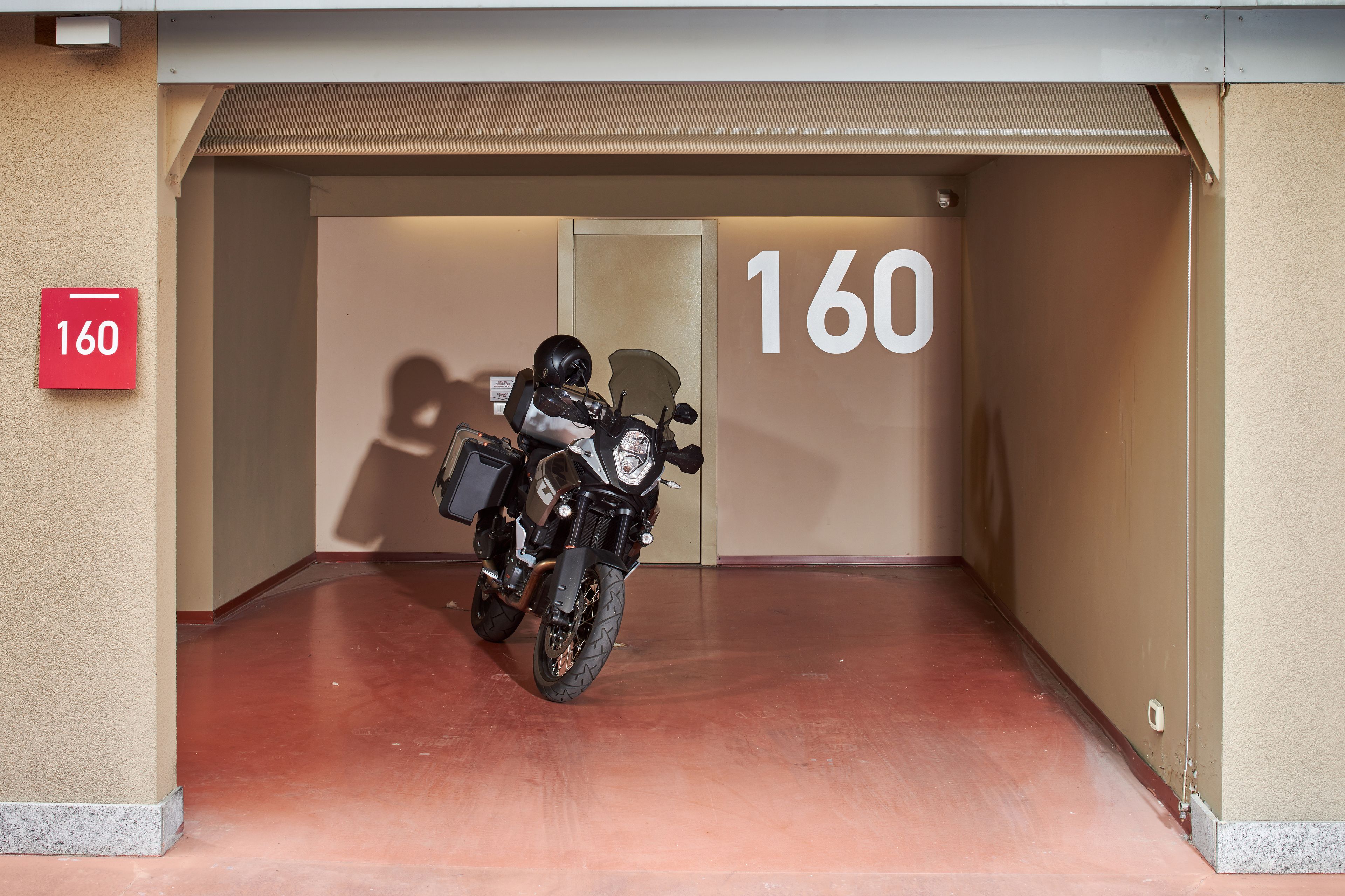 Une moto était garée à l’intérieur d’un bâtiment, et un panneau portant le numéro 160 était fixé au mur.