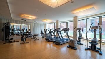 Un gimnasio amplio con diversas máquinas de cardio, zonas de pesas y un ventanal con vistas al exterior.